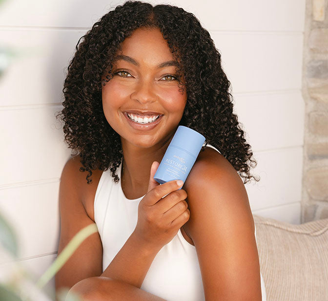 Smiling woman holding a blue RESTORE24  bottle with a neutral background