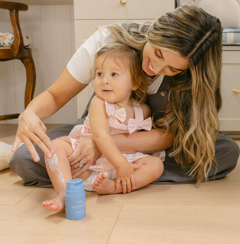Woman applying RESTORE24 cream to a child’s leg with the bottle beside them