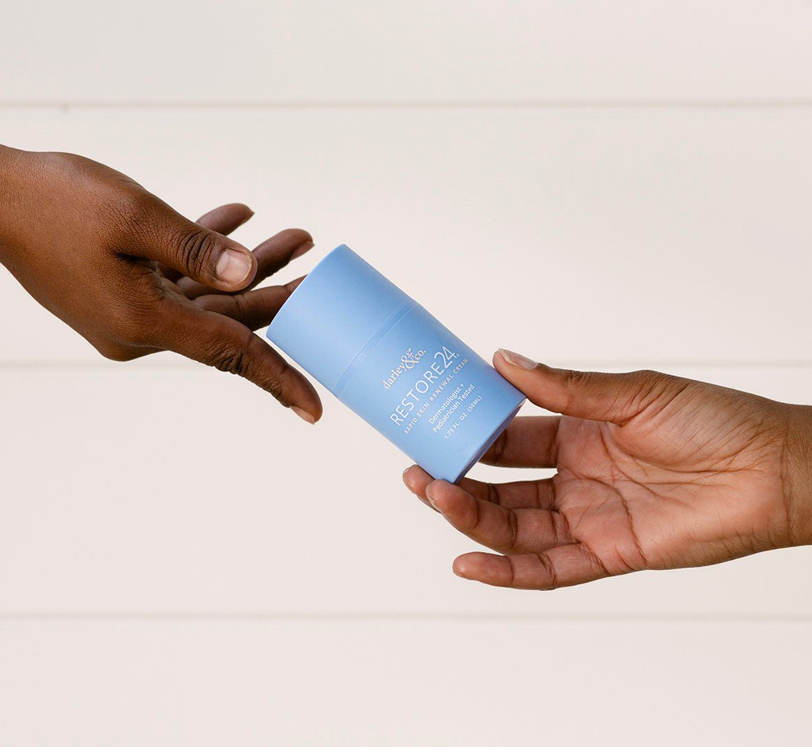 Two hands exchanging a blue RESTORE24 bottle on a plain background
